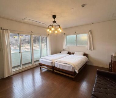 Twin beds on wooden floor with large sliding glass doors and simple seating at koyado kaziya, Iwate Tohoku