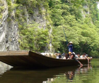 Passengers on a wooden flatboat guided by a standing boatman among green cliffs, koyado kaziya, Iwate Tōhoku