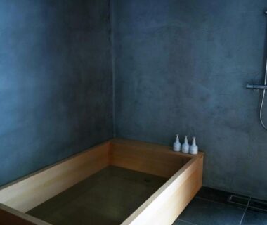 Wooden soaking tub in minimalist bathing room with wall shower and concrete walls