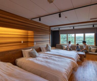 Three beds with white linens, wooden floors, window seating overlooking green landscape