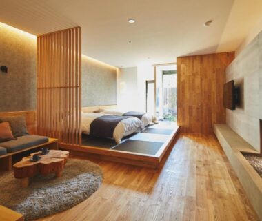 Spacious tatami platform with bed, sofa, wooden partition and garden-facing glass doors at nanaougi in Kanagawa