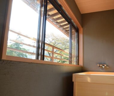 Wooden soaking tub beside window with balcony railing and garden view at nanaougi in Kanagawa