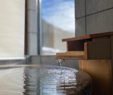 Round stone bath with wooden spout by window at Onogawaonsen Azumasou, Yamagata
