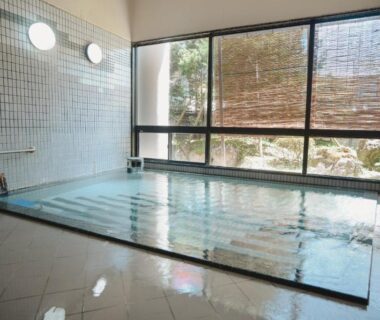 Tiled indoor onsen bath with large windows, bamboo blinds and garden view at Onogawa Onsen Azumasou Yamagata