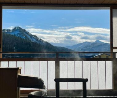 Indoor onsen bath framed by shoji and railing, wide window overlooking layered mountains at onogawaonsen azumasou, Yamagata