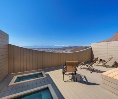 Rooftop wooden deck with two square onsen baths and lounge chairs at onsen hotel OMOTO, Nagano mountain view