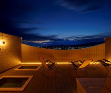 Wooden rooftop deck with two sunken baths and lounge chairs at onsen hotel OMOTO in Nagano, Chūbu