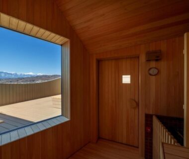 Wood-lined interior bathing room with large window framing mountain panorama at onsen hotel OMOTO, Nagano
