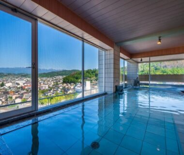 Indoor onsen bath with panoramic windows overlooking town and mountains at onsen hotel OMOTO Nagano