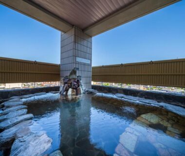 Stone-lined rooftop onsen bath with covered roof at onsen hotel OMOTO overlooking Nagano town