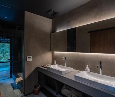 Double washbasins and illuminated mirror with doorway opening to greenery in ryugon bathroom, Niigata