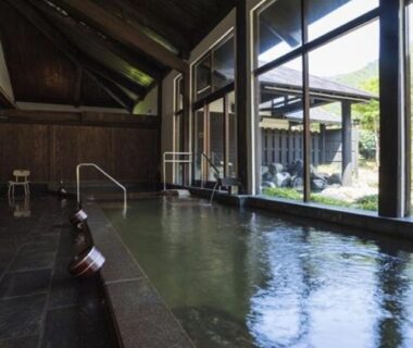 Indoor onsen with wooden interior, stone pool and floor-to-ceiling windows overlooking a garden courtyard at Ryugon in Niigata