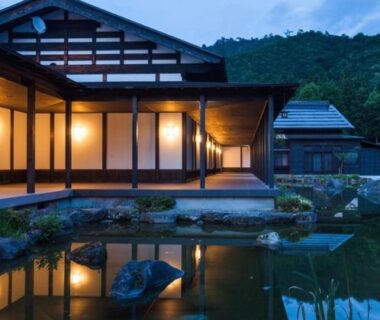 Traditional wooden ryokan with lit shoji veranda reflected in garden pond at ryugon in Niigata, Chūbu
