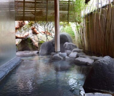 Rock-lined onsen with bamboo screen and garden greenery at soraichi ryokan in Miyagi