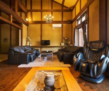 Wood-paneled lounge with leather sofas, massage chair, exposed beams and sunlit windows at Chalet de montagne Hibari d’Asagiri, Kumamoto