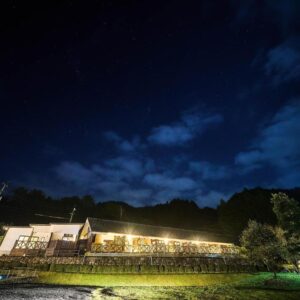 Warmly lit ryokan building at night with mountain silhouette, Chalet de montagne Hibari d’Asagiri, Kumamoto, Kyūshū