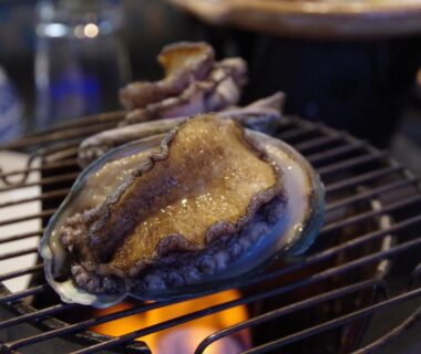 Whole abalone grilling on a wire grate over charcoal flame at Obama-sō ryokan in Toba, Mie