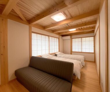 Tatami style guest room with two beds, shoji screens, exposed wooden beams and low sofa at Utsuboya-sō Tokyo