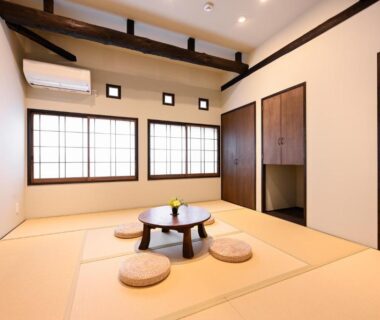 Tatami room with low round table, floor cushions, shoji windows and exposed wooden beams at Uribō Ryokan Nakamichi Urabō, Gunma