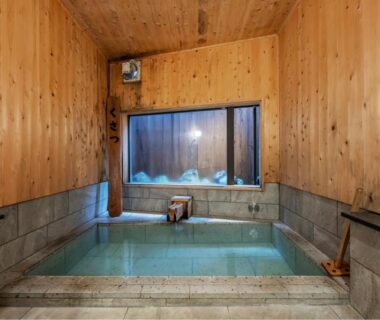 Indoor wooden onsen bath with stone edging and small window at Uribō Ryokan in Gunma, Kantō