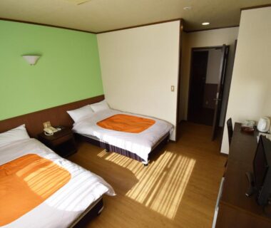 Twin beds with orange throws, wooden flooring, desk and TV in a bright room at Oyado Kokoro, Gifu