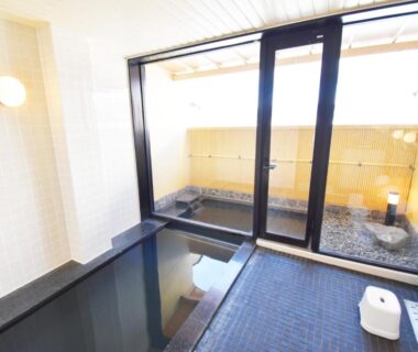 Indoor soaking tub with stool and sliding glass doors to small outdoor stone bathing area at Oyado Kokoro Gifu