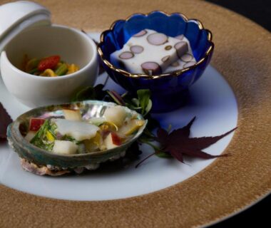 Ceramic bowls with octopus and seasonal vegetables on decorative platter with maple leaf garnish
