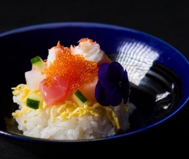 Japanese rice bowl topped with fish roe, shredded egg, cucumber and edible flower in a blue bowl