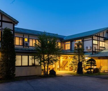 Lit traditional ryokan entrance with wooden facade and shoji windows at dusk, Kiyoshigekan, Gunma, Kantō