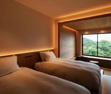 Twin beds in a serene Japanese-style room with large window overlooking wooded hills at Kuroshio Sō, Wakayama