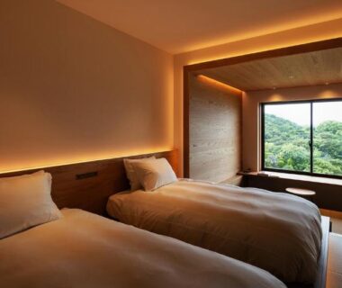 Twin beds with warm lighting, large window framing lush green hillside view at Kuroshio Sō in Wakayama