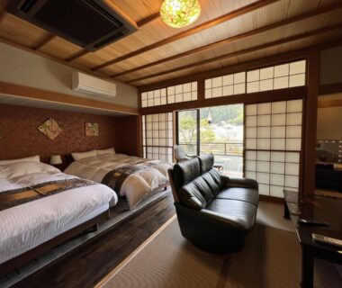 Tatami flooring, twin beds, sofa and shoji screens overlooking a small garden at Suikōen Sakura, Shizuoka