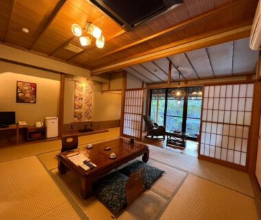 Tatami room with low table, zabuton cushions and shoji doors opening to garden at Suikōen Sakura, Shizuoka