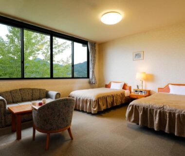 Twin bedroom with two beds, seating area and large window overlooking trees and hills at Miharu-en, Nara