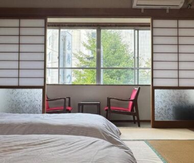 Tatami room with two low beds, shoji screens and seating by window overlooking greenery