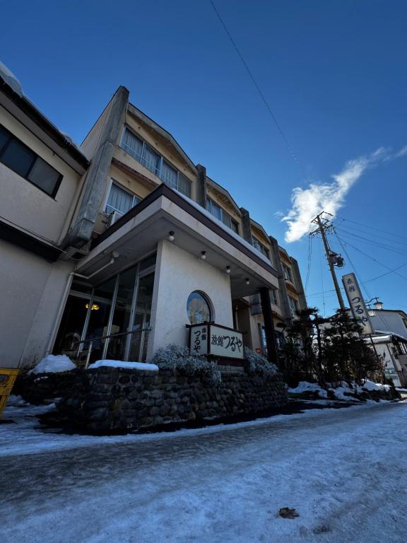 Snowy ryokan exterior Ryokan Tsuruya Nagano Snow-covered exterior of Ryokan Tsuruya with entrance and street under blue sky in Nagano, Chūbu