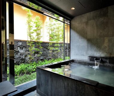 Indoor stone onsen bath overlooking small bamboo garden through sliding glass at Tsurukō in Ishikawa