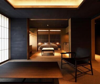 Minimal tatami interior with shoji screens, raised bed platform, low table and warm wooden lighting at Tsurukō, Ishikawa