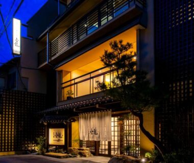 Illuminated traditional ryokan facade with noren, wooden lattice and balcony at dusk in Gifu, Chūbu region