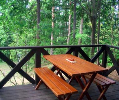 Outdoor wooden deck with table and benches overlooking tall trees at Yasuragi no Bettei Shikitei, Yamanashi
