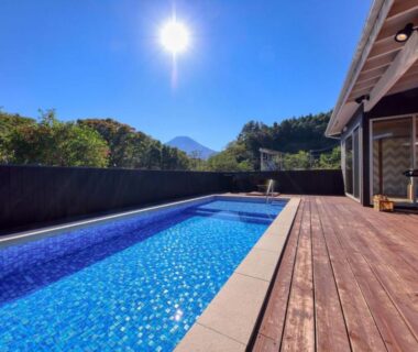 Outdoor pool beside wooden terrace at Grandome Fuji Oshino in Yamanashi with mountain backdrop and clear sky
