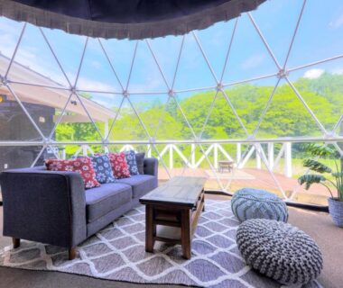 Geodesic dome lounge with sofa, poufs and wooden deck overlooking greenery at Grandome Fuji Oshino, Yamanashi
