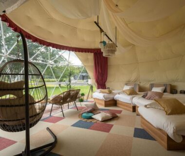 Interior of geodesic glamping dome with hanging chair, multiple beds and grassy view at Glamping Village Fuji Kawaguchiko Yamanashi