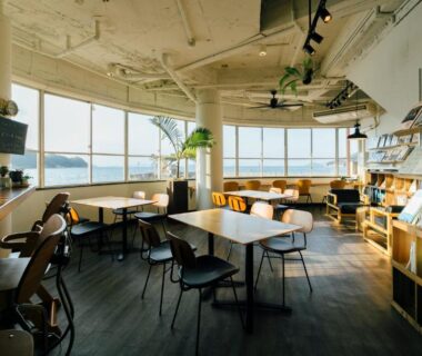 Lounge with floor-to-ceiling windows, tables and bookshelves at Seaside Katsuragahama-sō, Chūgoku Hiroshima