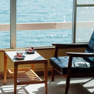 Two lounge chairs and a table with teacups by a large window overlooking the sea at Seaside Katsuragahama-sō