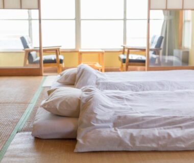 Futon bedding on tatami floor with large windows and low chairs, Seaside Katsuragahama-sō, Hiroshima
