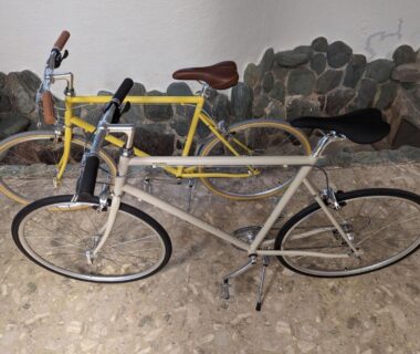 Two yellow and beige bicycles parked on pebble floor beside a stone wall at Seaside Katsuragahama-sō, Hiroshima