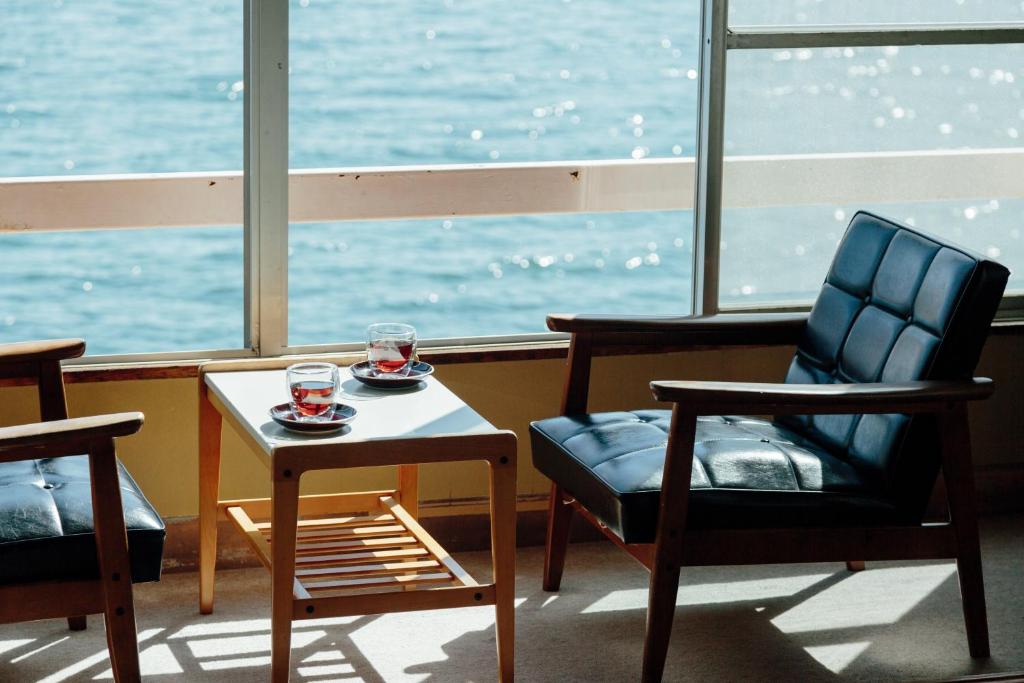 Window seating at Seaside Katsuragahama-sō Hiroshima Japan Two lounge chairs and a table with teacups by a large window overlooking the sea at Seaside Katsuragahama-sō