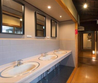 Long counter with three round sinks, mirrors, tiled wall and wooden corridor at Dozen Ryokan in Kyoto