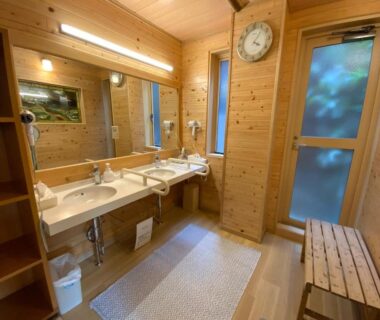 Wood-paneled washroom with double sinks, mirrors, wooden bench and frosted window at Business Inn Haijima Tokyo